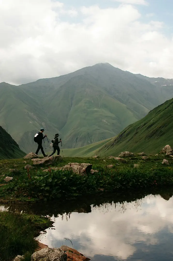 Deux trekkeurs en pleine ascension dans un paysage de montagne verdoyant — immersion totale dans une aventure Trekks, entre exploration sauvage et progression gamifiée à travers des défis physiques, XP et badges à débloquer.