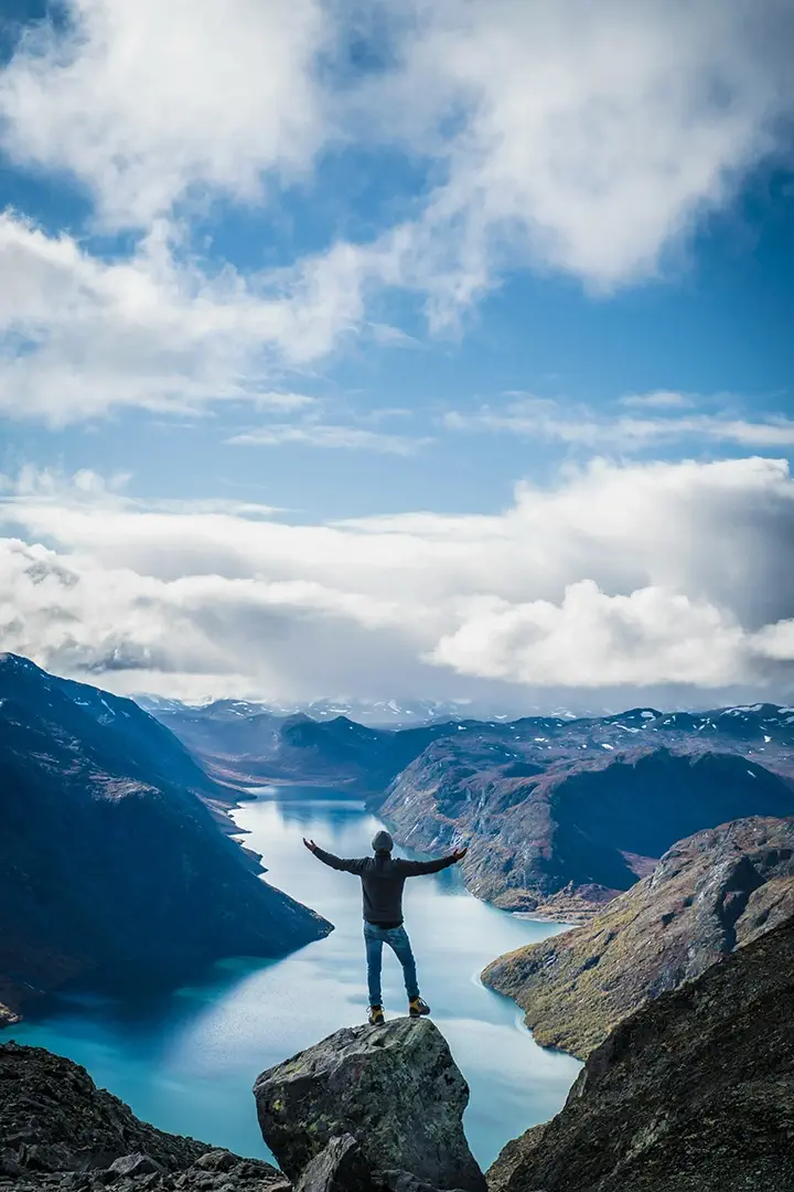 Trekkeur triomphant au sommet d’une falaise surplombant un fjord alpin — symbole d’accomplissement d’une mission Trekks, entre challenge personnel, récompense immersive et quête grandeur nature dans un univers inspiré des jeux de rôle.